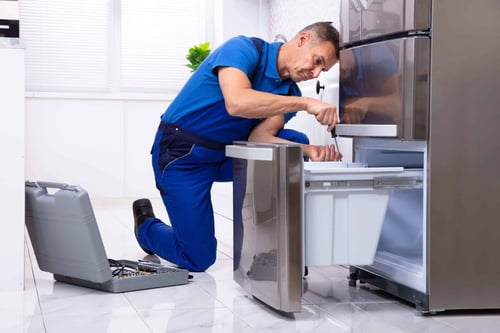 The engineer in the blue uniform is repairing the refrigerator