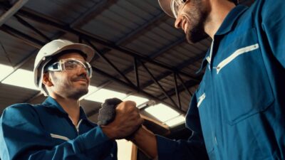 Two colleagues in overalls chatting and shaking hands